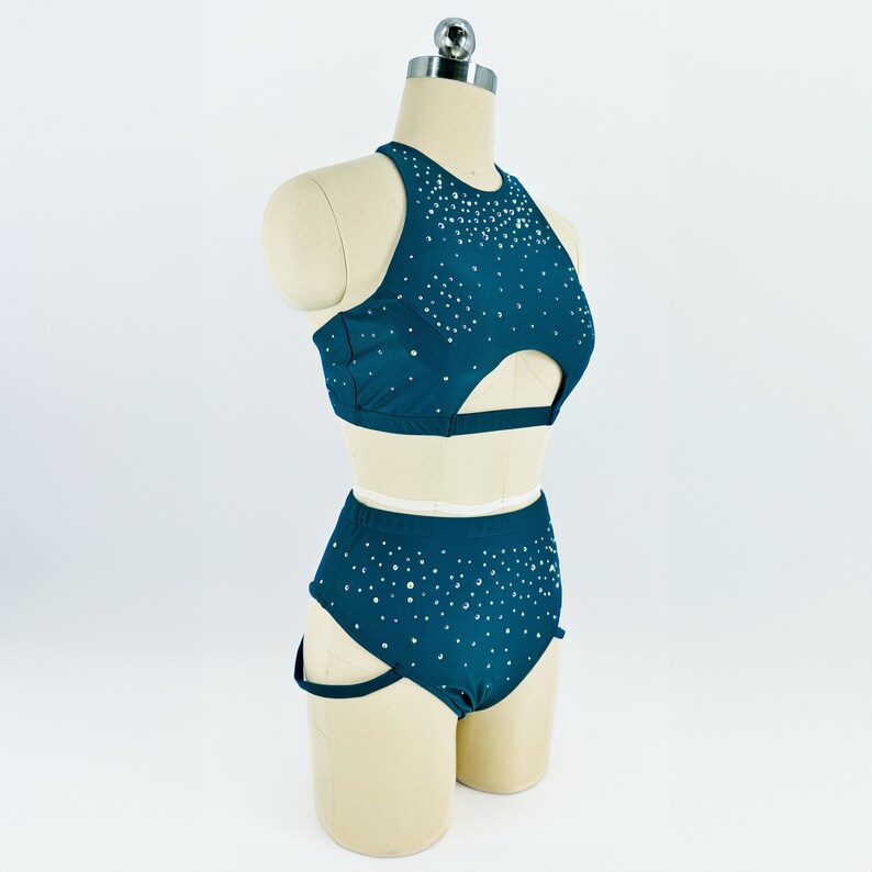 May include: A teal dance outfit with a halter top and high-waisted shorts. Both pieces are covered in small, sparkly rhinestones.