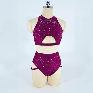 May include: A burgundy two-piece dance costume with a halter top and high-waisted shorts. Both pieces are covered in small, silver rhinestones.