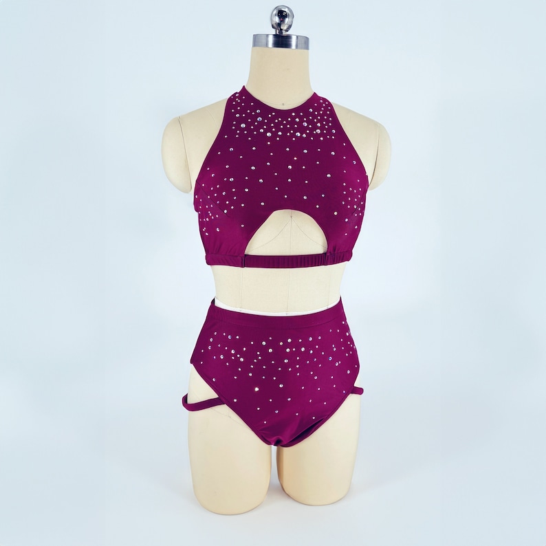 May include: A burgundy two-piece dance costume with a halter top and high-waisted shorts. Both pieces are covered in small, silver rhinestones.
