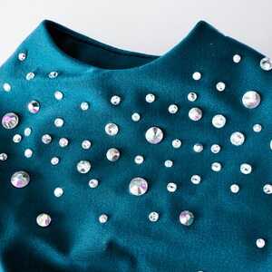 May include: A teal blue fabric garment with a scoop neck and a scattered pattern of iridescent rhinestones.