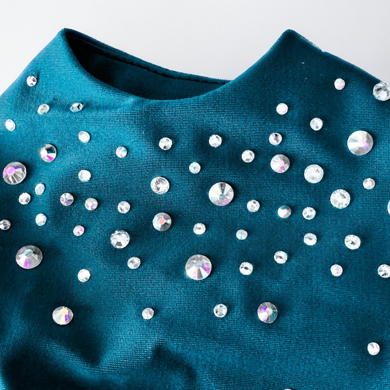 May include: A teal blue fabric garment with a scoop neck and a scattered pattern of iridescent rhinestones.