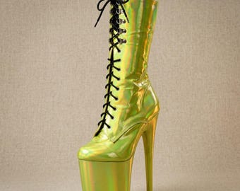 Op de afbeelding: Een kuitlaars met een reflecterende, iriserende limoengroene afwerking. De laars heeft een hoge plateauzool, een dunne stilettohak en een vetersluiting aan de voorzijde met zwarte veters door zilverkleurige metalen oogjes en haken.