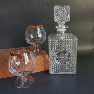 May include: A set of three clear glass decanters with a textured surface. The decanters have a gold rim and are in a wooden box. The box has the text "Number Two" on it.