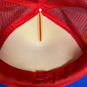 May include: The inside of a red and blue mesh trucker hat. The hat has a white mesh lining and a red adjustable strap.