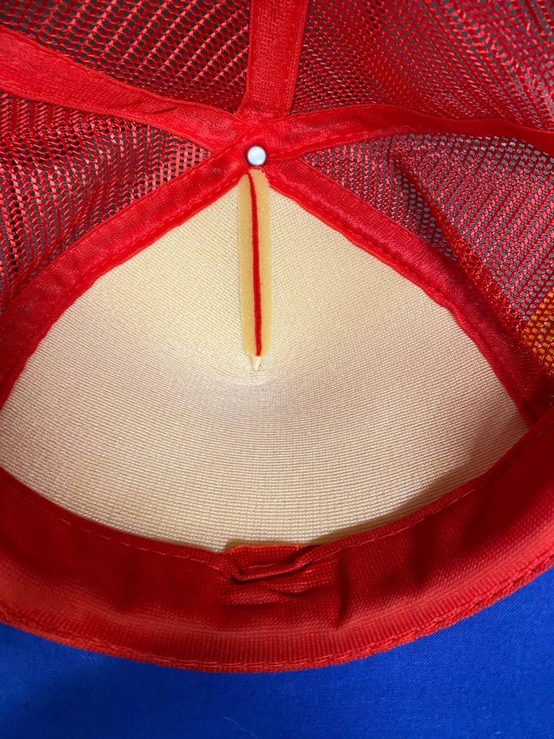 May include: The inside of a red and blue mesh trucker hat. The hat has a white mesh lining and a red adjustable strap.