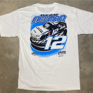 May include: White t-shirt with a blue and white graphic of a race car with the number 12 and the name "Ryan Newman" printed on the back.