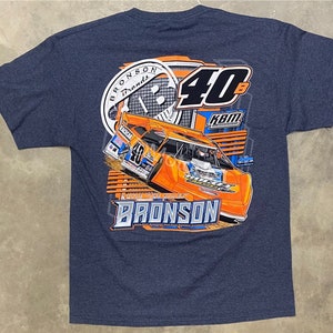 May include: A navy blue t-shirt with a graphic of a race car on the back. The car is orange and black with the number 40 on the side. The text "Bronson Brands" and "40B KBM" are also on the shirt.