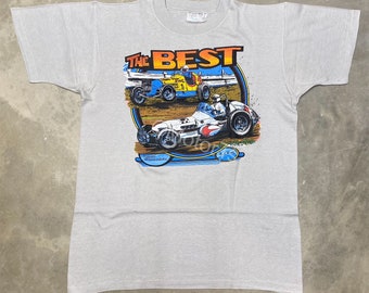 May include: A grey t-shirt featuring a graphic of two racing cars on a track. The text "THE BEST" is printed above the cars. The text "Danny  Hamannshitz" is printed below the cars.