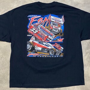 May include: Black t-shirt with a graphic of a race car driver, Jared Eshelman, with the number 39 on the car. The car is on a blue and white track with the text "Willow Street Pennsylvania" at the bottom.