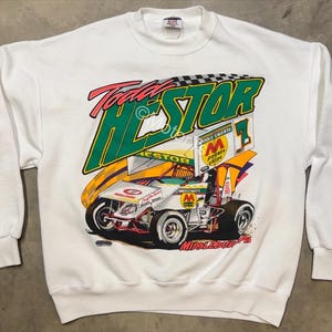 May include: White crewneck sweatshirt featuring a colorful graphic of a race car with the text "Todd HESTOR" in green and red. The design includes a checkered flag and sponsor logos. The sweatshirt has long sleeves.