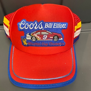 May include: Red, white, and blue trucker hat with a Coors Light logo and the text "Bill Elliott Winston Cup Champion". The hat features a small embroidered image of a race car with the number 9.