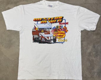 May include: White t-shirt with a vibrant graphic of a race car, the text "WESTERN WORLD VALVOLINE", and "MANZANITA SPEEDWAY ARIZONA Coors". The design incorporates flags and a racing theme.