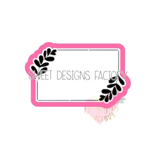 May include: A pink rectangular frame with black leaf designs on each corner. The text "SWEET DESIGNS FACTORY" is centered inside the frame.