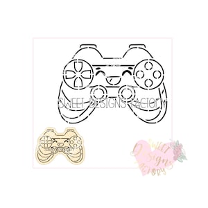 May include: A black and white outline of a video game controller with a smiling face. The controller has a directional pad, four buttons, and two joysticks. The text "SWEET DESIGNS FACTORY" is below the controller.