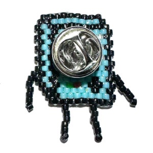 May include: A black and blue beaded pin of a cartoon character with a square body and legs. The pin has a metal clasp on the back.