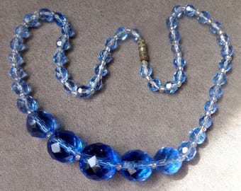 May include: A blue glass beaded necklace with larger, faceted blue beads in the centre.