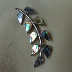 May include: A silver brooch with a branch design featuring iridescent abalone shell leaves.