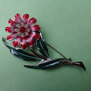 May include: A red and white enamel flower brooch with a rhinestone center and green enamel leaves.