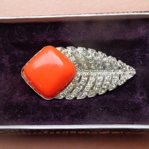 May include: A silver brooch featuring a bright orange square stone set in the centre and a leaf design encrusted with rhinestones.