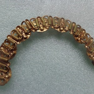 May include: A gold-toned bracelet with a repeating pattern of linked rectangular and circular elements. The bracelet is curved, suggesting it is flexible and designed to fit the wrist. The metal has a polished finish.