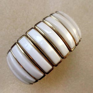 Peut inclure: Un bracelet extensible blanc et or avec une série de panneaux blancs rectangulaires séparés par des bandes dorées.