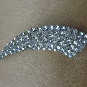 May include: A silver-toned brooch shaped like a curved blade, entirely covered in clear rhinestones.