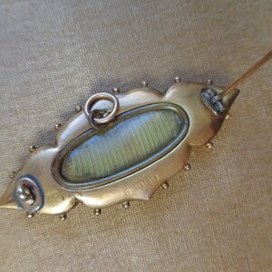 May include: Gold-toned brooch with a decorative, leaf-shaped design. The brooch has a glass oval in the centre and a pin on the back. The back of the brooch is marked with the number "0161391".