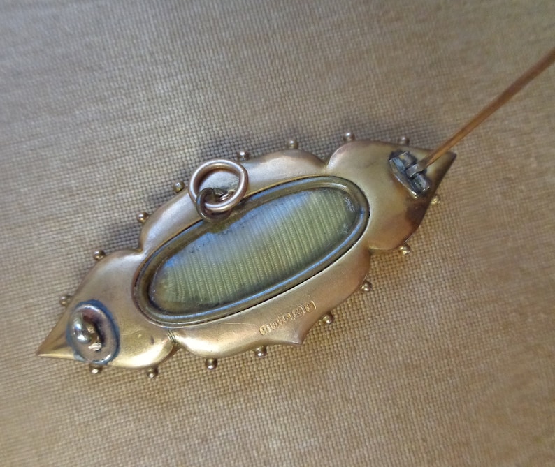 May include: Gold-toned brooch with a decorative, leaf-shaped design. The brooch has a glass oval in the centre and a pin on the back. The back of the brooch is marked with the number "0161391".