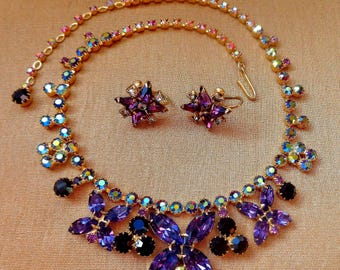 May include: A vintage jewellery set comprising a necklace and matching earrings. The necklace and earrings are decorated with purple, black, and iridescent rhinestones set in gold-tone metal. The necklace has a floral design.