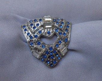 May include: A silver brooch with a geometric design featuring blue and clear rhinestones.