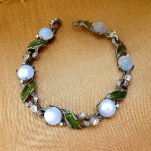 May include: A silver tone bracelet with blue glass stones and green enamel leaves. The bracelet has a clasp closure.