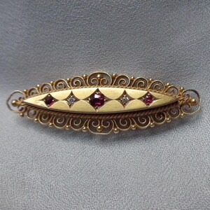 May include: A gold filigree brooch with a central oval panel set with three red gemstones and two clear gemstones.