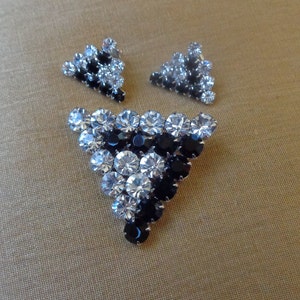 May include: A set of vintage black and clear rhinestone earrings and brooch. The brooch is shaped like a triangle and features a cluster of black and clear rhinestones.
