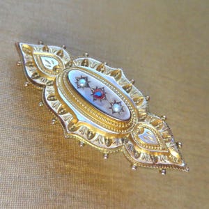 May include: A gold brooch with a white cameo set in a gold filigree frame. The cameo features three red and white gemstones.