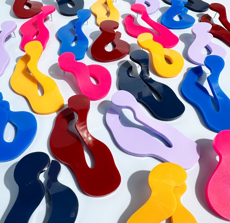 Pode incluir: Uma variedade de brincos coloridos em forma abstrata em v&aacute;rios tons, incluindo amarelo, rosa, azul e vermelho. Cada brinco tem um pino para orelhas furadas. Os brincos est&atilde;o dispostos sobre uma superf&iacute;cie branca, criando uma exibi&ccedil;&atilde;o vibrante de joias modernas.