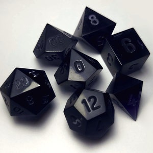 May include: Set of seven black polyhedral dice with white numbers. The dice are in various shapes, including a d20, d12, d10, d8, d6, and d4.