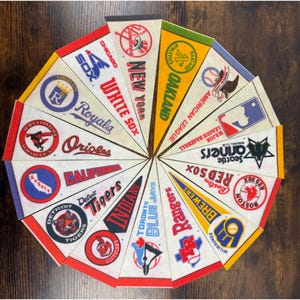 May include: A collection of triangular felt pennants featuring various Major League Baseball team logos and names, including the New York Yankees, Chicago White Sox, Kansas City Royals, Baltimore Orioles, Detroit Tigers, and Toronto Blue Jays.