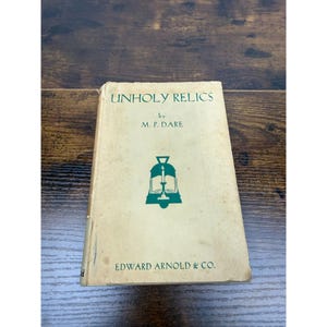 May include: A vintage book titled "Unholy Relics" by M. P. Dare. The cover is off-white with green text and a green illustration of a candle, book, and bell. The publisher's name, Edward Arnold & Co., is printed at the bottom.