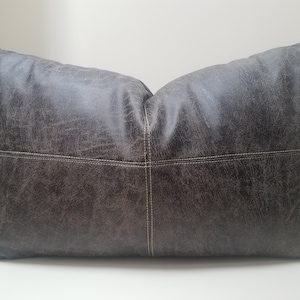 May include: A dark gray rectangular pillow with a distressed leather look and white stitching. The pillow has a slightly textured surface.