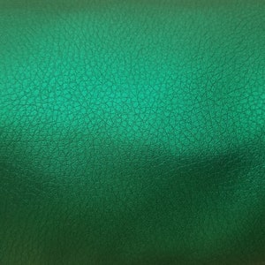 K&ouml;nnte beinhalten: Nahaufnahme einer strukturierten, gr&uuml;nen Lederoberfl&auml;che. Das Leder hat einen dezenten Glanz und eine leicht unebene Textur.