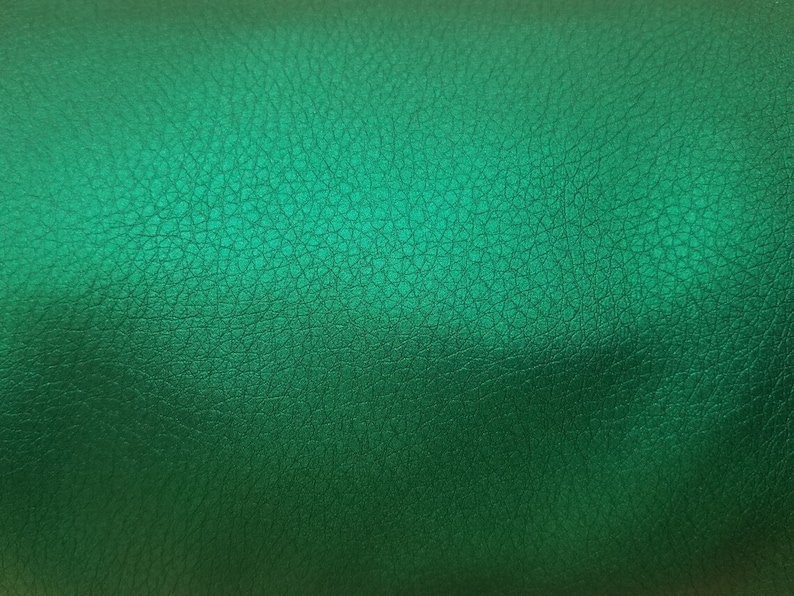 K&ouml;nnte beinhalten: Nahaufnahme einer strukturierten, gr&uuml;nen Lederoberfl&auml;che. Das Leder hat einen dezenten Glanz und eine leicht unebene Textur.