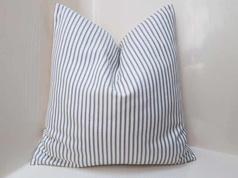 Puede incluir: Una almohada blanca con rayas azules. La almohada est&aacute; hecha de una tela suave y tejida y tiene un dise&ntilde;o simple y cl&aacute;sico.