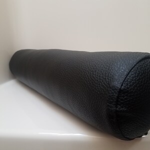 May include: A black cylindrical pillow with a textured leather-like cover.