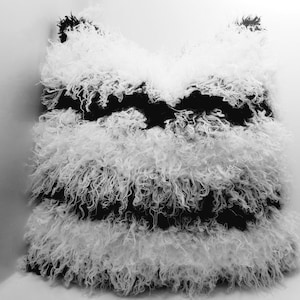 May include: A black and white striped throw pillow with a fluffy, shaggy texture. The pillow is made of a soft, plush material and has a unique, eye-catching design.