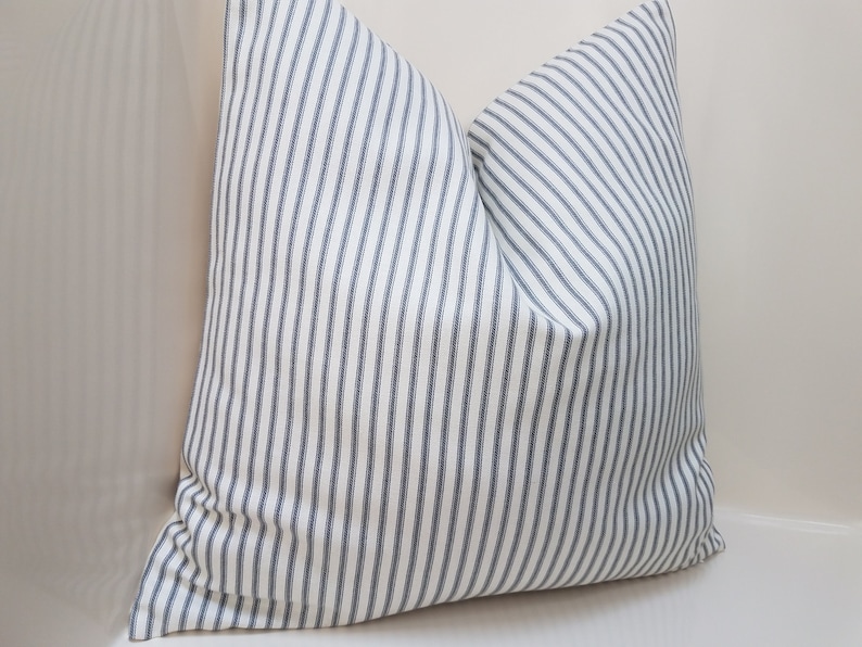 Puede incluir: Una almohada blanca con rayas azules. La almohada est&aacute; hecha de una tela suave y tejida y tiene un dise&ntilde;o simple y cl&aacute;sico.