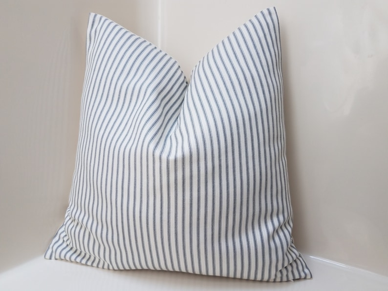 Puede incluir: Una almohada blanca con rayas azules. La almohada est&aacute; hecha de una tela suave y tejida y tiene un dise&ntilde;o simple y cl&aacute;sico.
