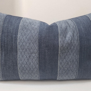 May include: Rectangular denim pillow with a patchwork design. The pillow features vertical stripes of varying denim textures, including a diamond pattern, all in shades of blue. White stitching accents the seams.