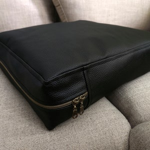 K&ouml;nnte beinhalten: Schwarzes Lederkissen mit Rei&szlig;verschluss. Das Kissen liegt auf einem hellgrauen Sofa.