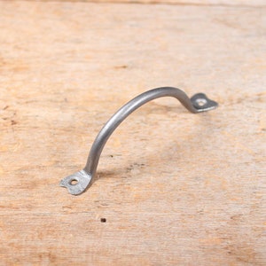 May include: A silver metal handle with a curved shape and heart-shaped ends. The handle is on a wooden surface.