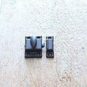 May include: Black metal door latch with a round knob. The latch is in two pieces, a square piece with the knob and a rectangular piece.